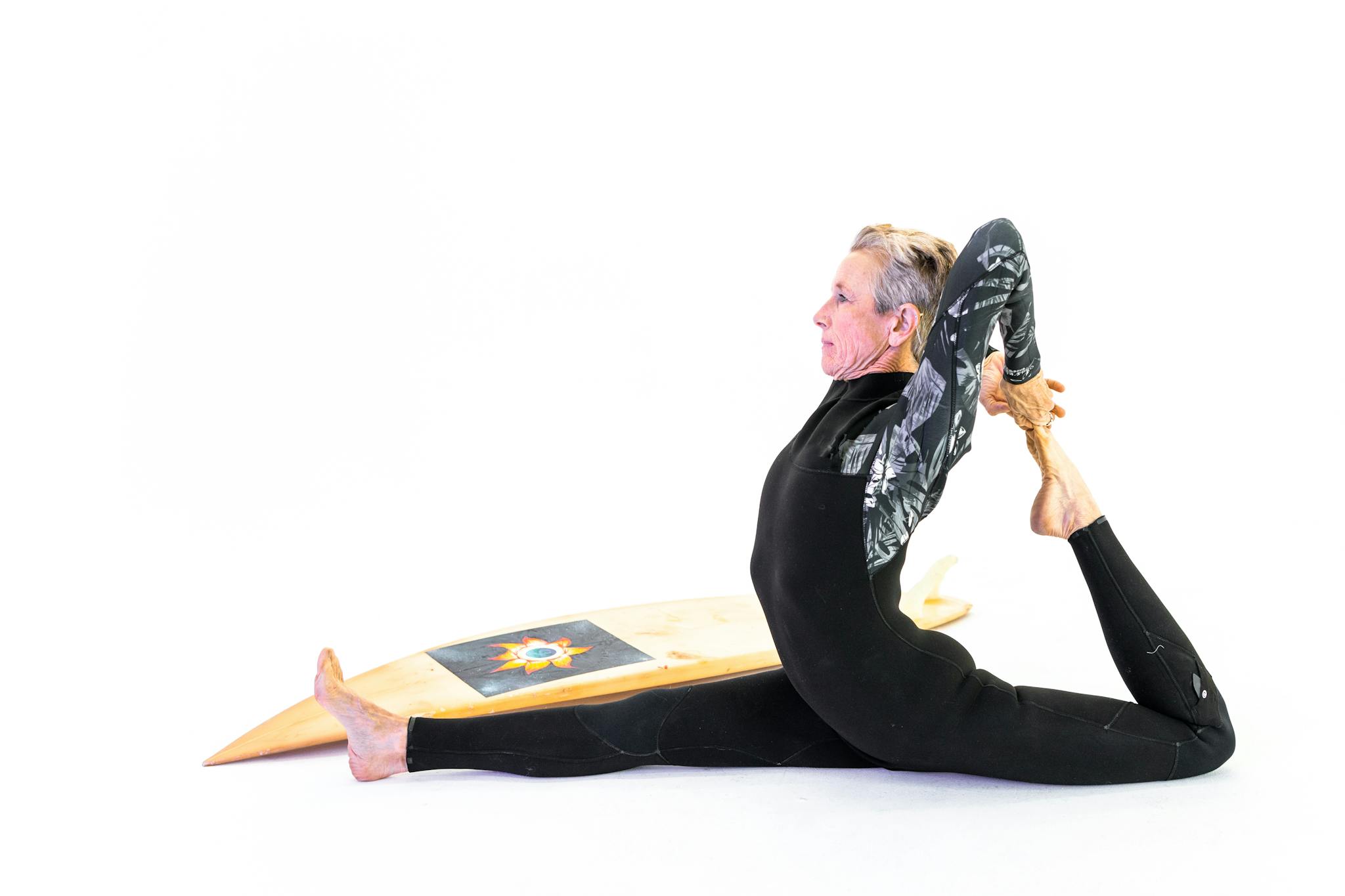 Woman Doing Stretching Exercise Beside A Surfboard